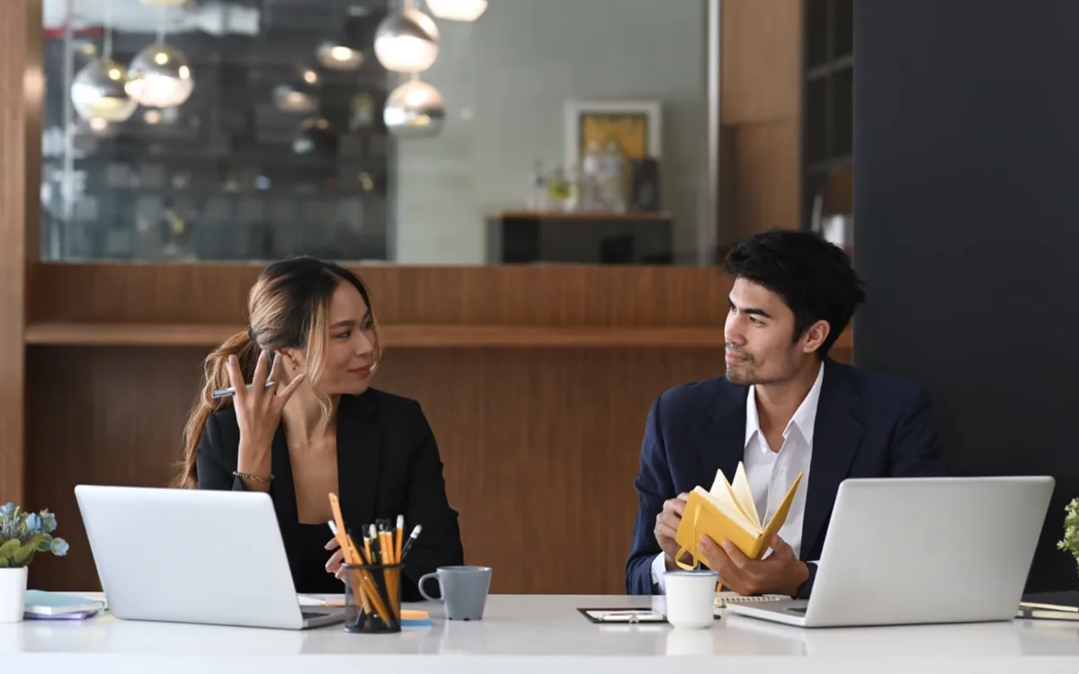 Two people comparing notes across a shared workspace
